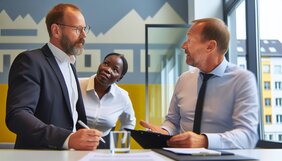 Sachverständiger und Finanzberater besprechen gemeinsam eine Immobilienbewertung am Tisch mit Unterlagen
