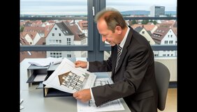 Europäischer Sachverständiger prüft Grundrisse eines Mehrfamilienhauses mit Dachgeschossausbau in einem deutschen Büro