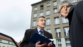 Sachverständiger im Gespräch mit Eigentümer vor Bestandsgebäude